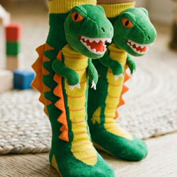 Children's feet wearing green dinosaur-themed socks on a wooden floor.